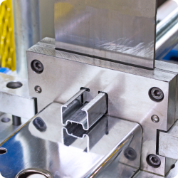 Industrial metal extrusion process showing a profile being pressed through a custom-shaped die.