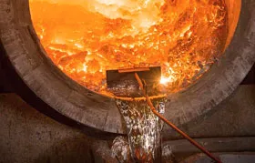 The interior of a large industrial aluminum smelting furnace, with a tool sampling the turbulent, glowing molten metal, illustrating the primary production phase of aluminum manufacturing where bauxite is converted to liquid aluminum.