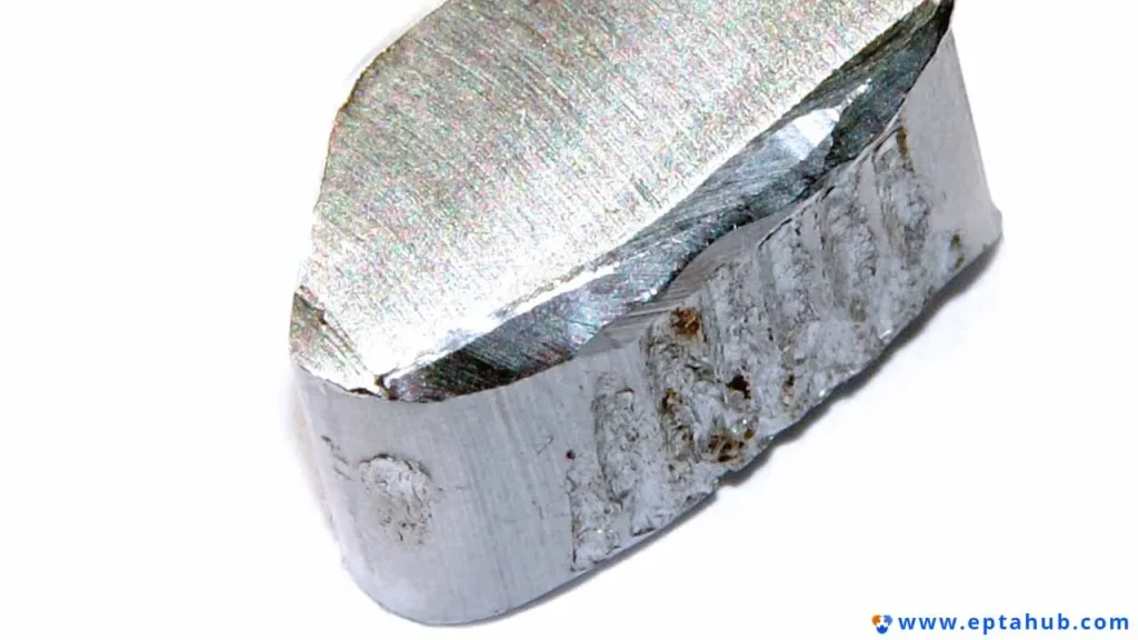 Uma macrofotografia de um pedaço de alumínio fraturado, revelando a estrutura cristalina dos grãos da falha dúctil do metal, uma característica fundamental na ciência dos materiais e na análise de engenharia.